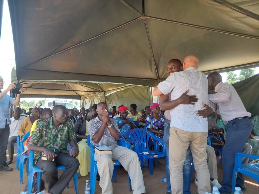 Henk spreekt voor groep mensen en omarmt een man